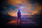 A man standing triumphant on a beach in New Romney while looking out into the water