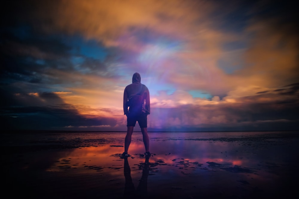 A man standing triumphant on a beach in New Romney while looking out into the water