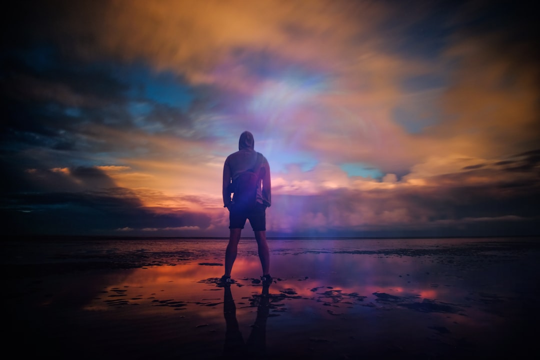 A man standing triumphant on a beach in New Romney while looking out into the water, Endless