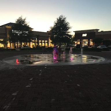 Evening shot of the retail plaza with warm lighting and customers walking.
