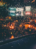 A cinematic frame showing a blurred cityscape at dusk through a rain-speckled window.
