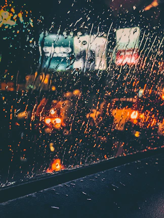 A cinematic frame showing a blurred cityscape at dusk through a rain-speckled window.