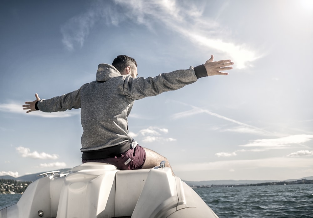 man in gray hoodie sitting on white boat during daytime