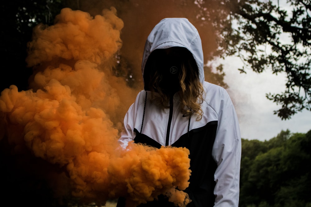woman in black and white zip-up hoodie near orange smokes under a tree