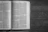 An open book lies on a wooden surface, displaying pages filled with dense text in a serif font. The book appears to be well-worn, with slightly curved pages and a textured cover. The wooden surface beneath has a rough, natural finish with visible grain patterns.
