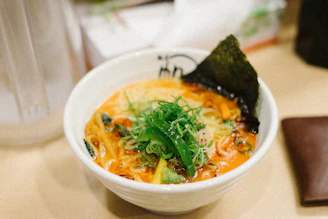 A steaming bowl of fusion ramen with rich broth, noodles, and colorful toppings.