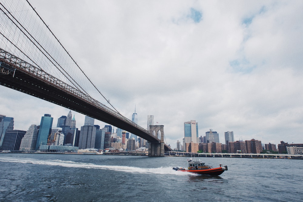 rotes Schnellboot fährt auf dem Wasser unter der Brooklyn Bridge hindurch