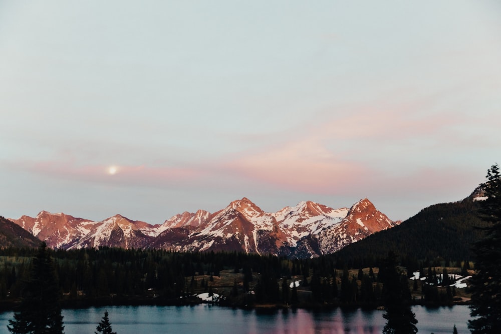 body of water across snow covered mountain under cloudy sky