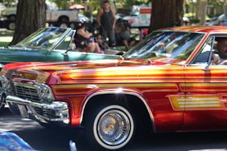 A vibrant scene of a vintage red, white, and blue classic car parked at a lively outdoor car show with people admiring the vehicles.