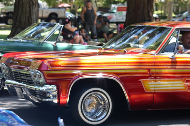 A vibrant scene of a vintage red, white, and blue classic car parked at a lively outdoor car show with people admiring the vehicles.