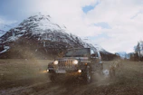 A rugged 4x4 vehicle climbing a steep, muddy hill under a cloudy sky.