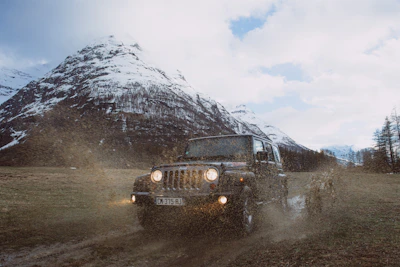 A rugged 4x4 vehicle climbing a steep, muddy hill under a cloudy sky.