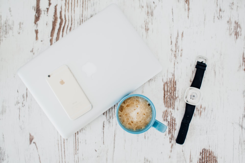 a cup of coffee next to a smart phone and a watch