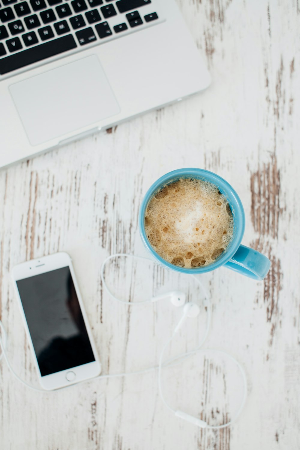 An overhead shot of a cup of coffee next to an iPhone and a MacBook