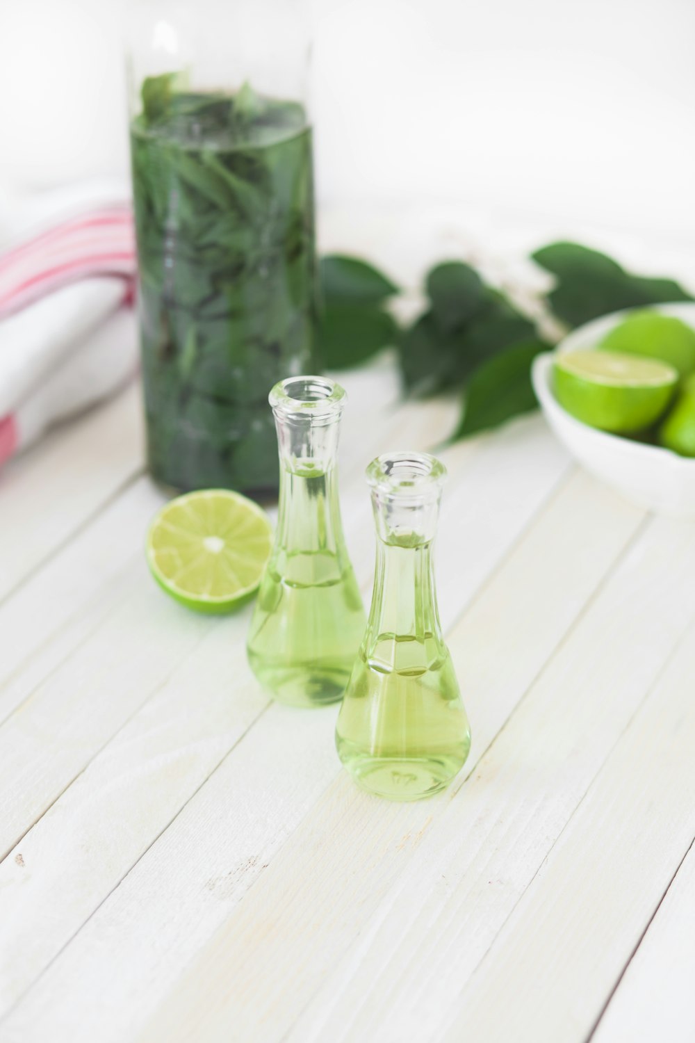 two clear glass bottles with lime juice on white wooden table