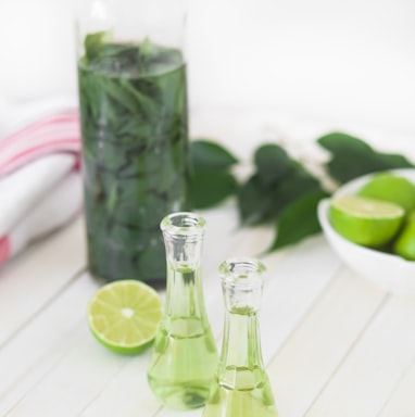 two clear glass bottles with lime juice on white wooden table