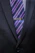Close-up of a finely knotted silk tie in deep navy blue with subtle texture, draped over a tailored suit jacket.