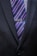 A close-up of a person wearing a dark suit jacket with a tie featuring diagonal stripes in blue, pink, and purple shades. A tie clip reading 'Grandpa' is attached to the tie.