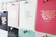 A collection of motivational quotes displayed on different colored cards pinned to a board. Each card has gold lettering featuring different inspirational sayings. The board is organized with silver pins holding the cards in place.