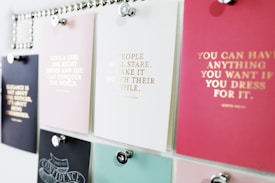 A collection of motivational quotes displayed on different colored cards pinned to a board. Each card has gold lettering featuring different inspirational sayings. The board is organized with silver pins holding the cards in place.