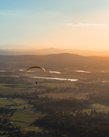 Paraglider soaring over the lush green hills of Poggio Bustone at sunset.