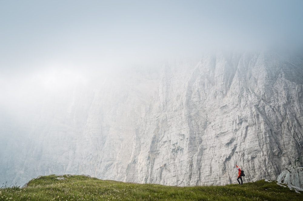 person standing on green grass field beside white high mountain under white sky during daytime