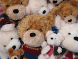 A collection of plush teddy bears with varying shades of brown and cream fur. They are grouped together in a cozy arrangement and some are wearing colorful knitted scarves.