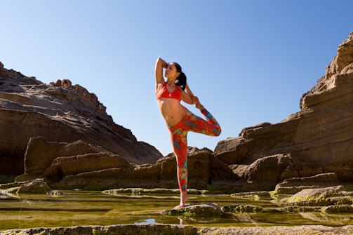 A hiker practicing yoga on a rocky outcrop overlooking a vast valley.