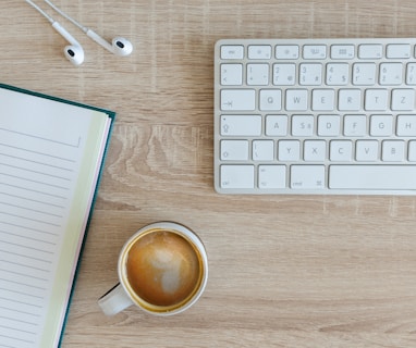 teclado de computador perto de caderno e xícara de café sobre a mesa