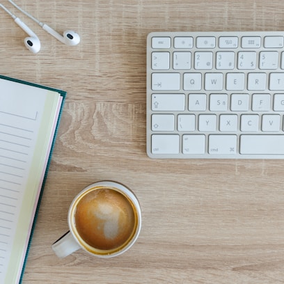 coffee latte near white wireless keyboard and Apple EarPods on the table photography