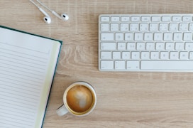 coffee latte near white wireless keyboard and Apple EarPods on the table photography