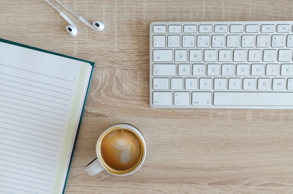 café con leche cerca de teclado inalámbrico blanco y Apple EarPods en la fotografía de la mesa