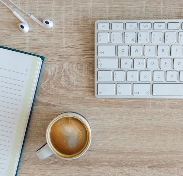 coffee latte near white wireless keyboard and Apple EarPods on the table photography