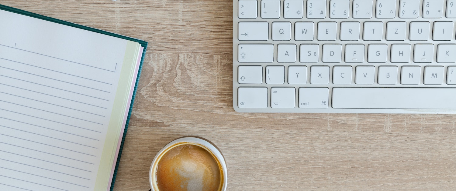 coffee latte near white wireless keyboard and Apple EarPods on the table photography