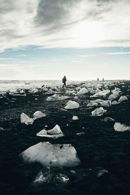person walking beside body of water during daytime in Jökulsárlón Iceland