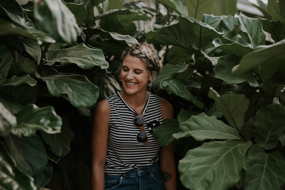 woman wearing black and white striped sleeveless shirt surrounded by green plants smiling posting for photo