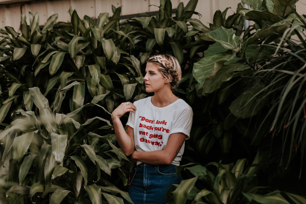 woman in white shirt standing and surrounded by green plants