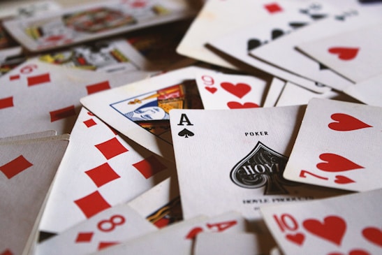 A scattered pile of playing cards featuring various suits such as hearts, diamonds, and spades is prominently visible. The Ace of Spades is in the foreground, along with the nine and ten of hearts.