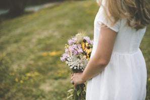 A serene outdoor setting with a bride holding a bouquet of white flowers.