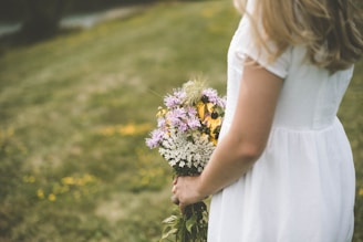 A serene outdoor setting with a bride holding a bouquet of white flowers.