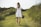 woman holding ukulele while walking on grass field surrounded with tall grasses
