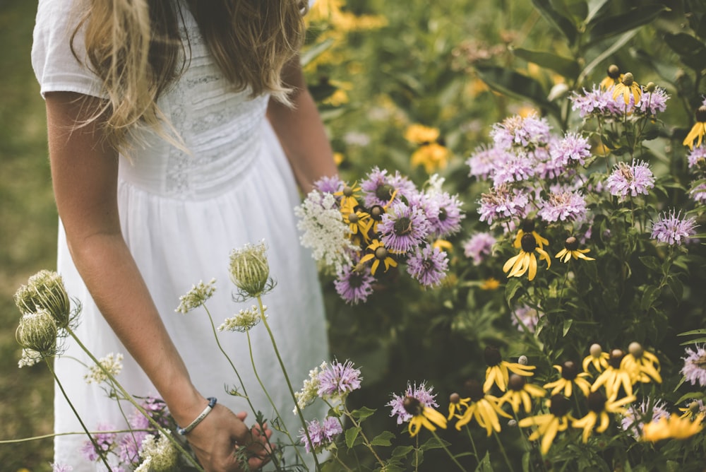 Frau trägt weißes Kleid und pflückt Blütenblätter