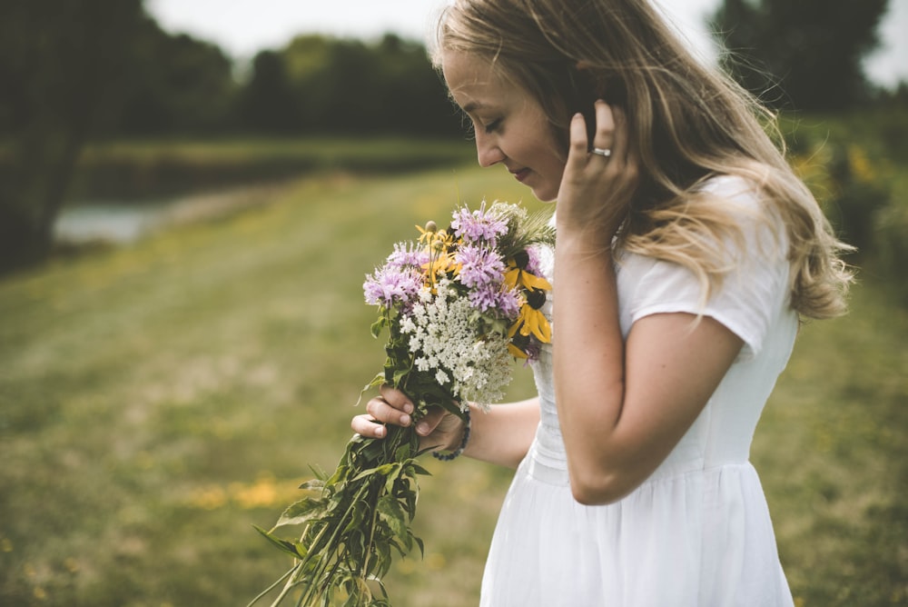 woman wearing white shirt holding flower wile smelling