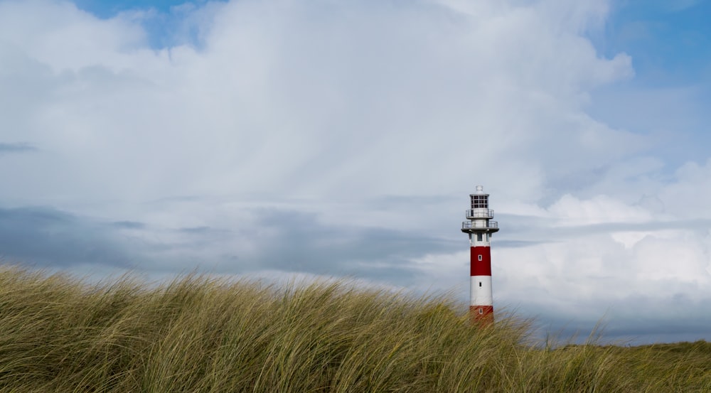 white and red lighthouse near grassland under white clouds at daytime