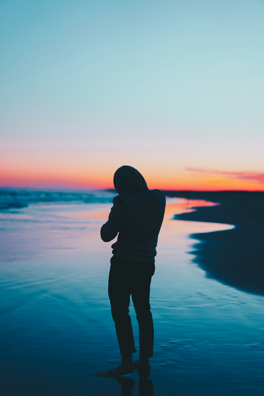 silhueta do homem em pé na costa durante o pôr do sol