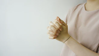 person wearing pink crew-neck shirt with hand clasped together