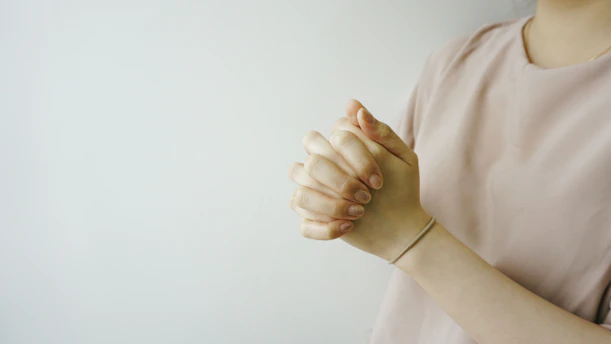 person wearing pink crew-neck shirt with hand clasped together