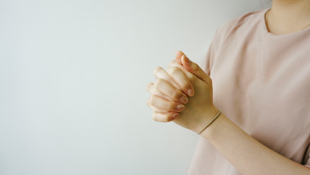 person wearing pink crew-neck shirt with hand clasped together