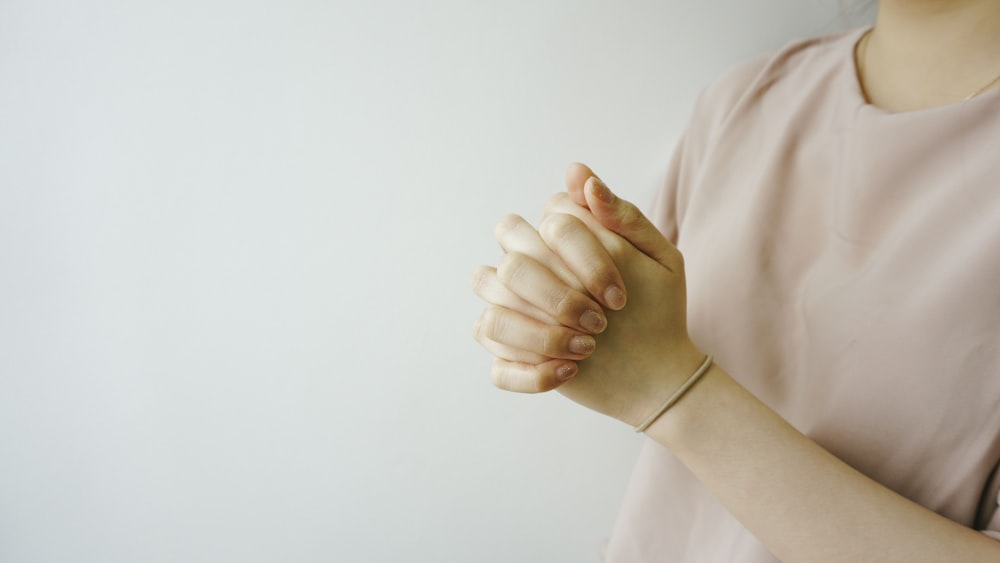 person wearing pink crew-neck shirt with hand clasped together