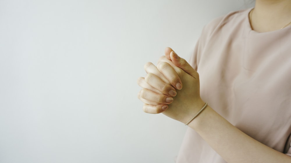 Persona que viste una camisa rosa de cuello redondo con la mano entrelazada